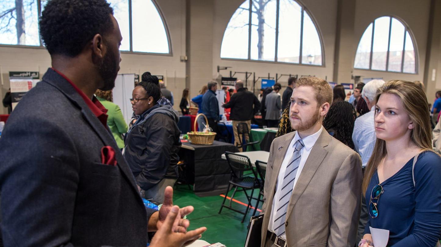 Two students at a career fair, speaking with a potential employer.