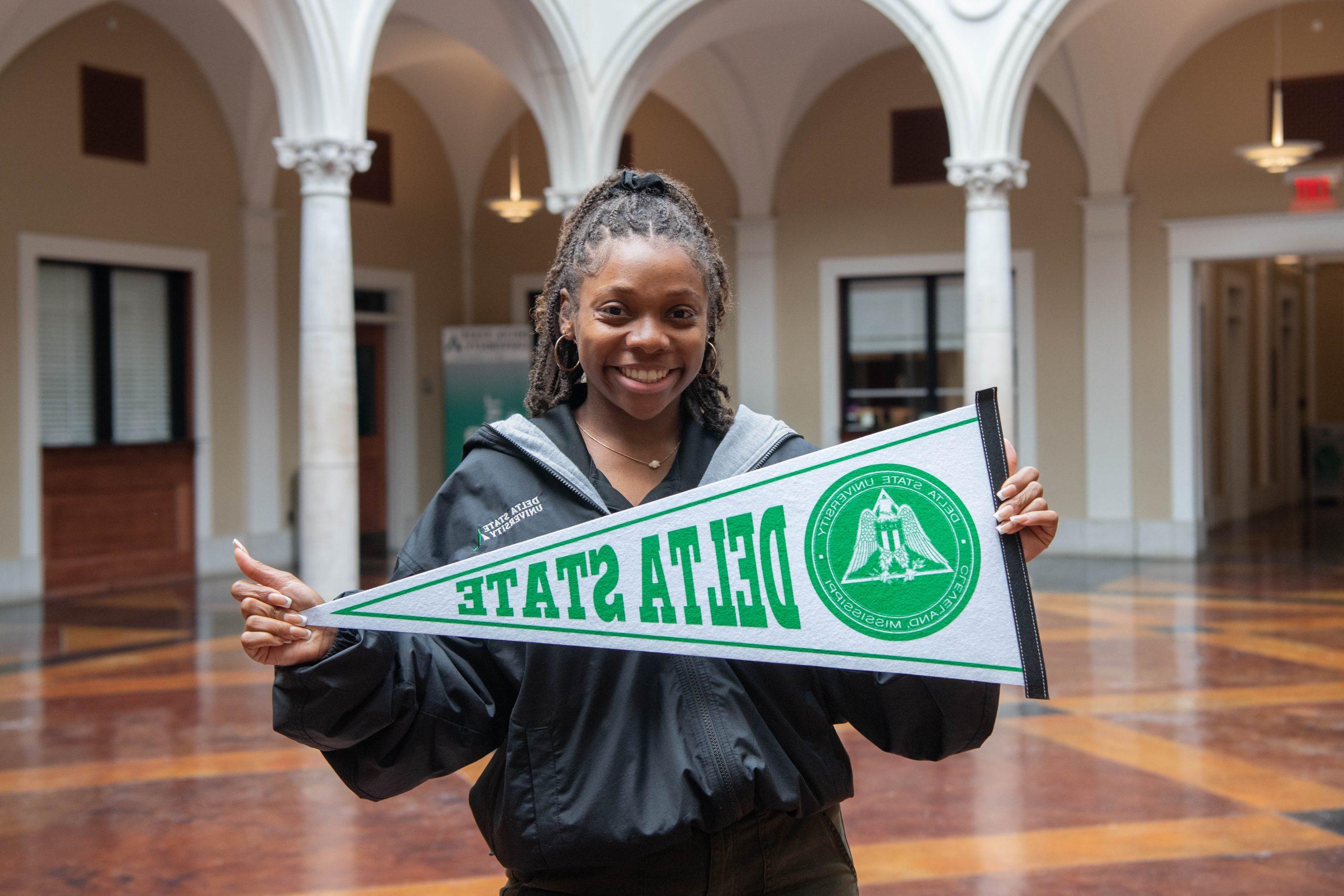 招生 recruiter holding Delta State pennant in the administration building.